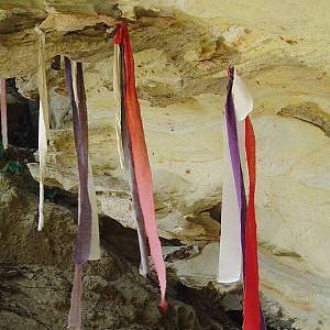 Photo shows strips of red cloth hanging from a cave ceiling