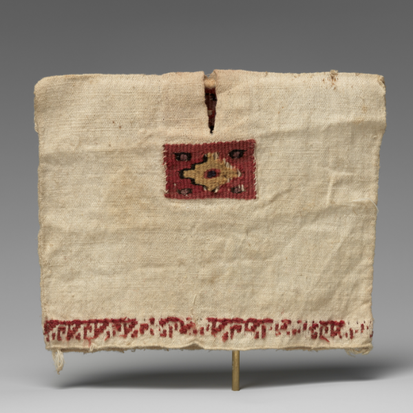 A tan colored tunic stretched to show the height and width. The tunic has a simple slit for the neck, a red and brown geometric design along the chest, and red embroidery along the hem. 